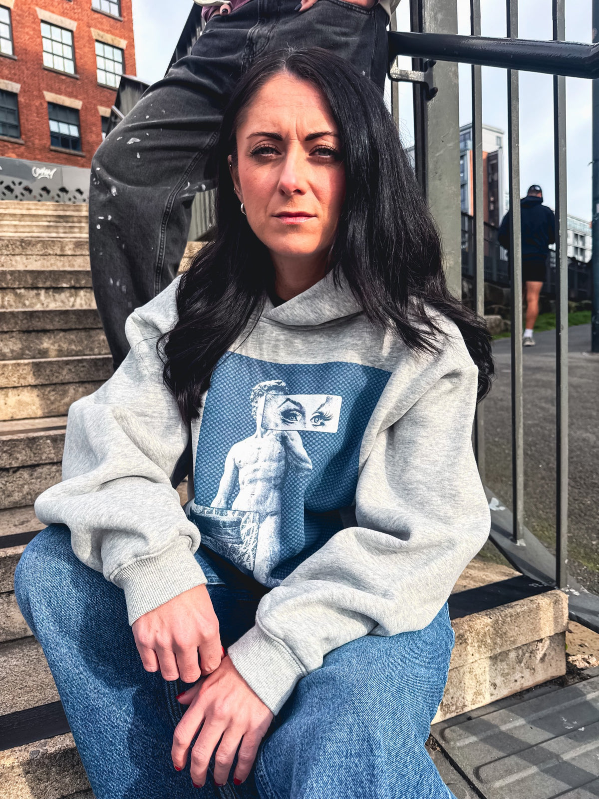Model wearing the grey Proud in the City hoodie, showing the blue collaboration artwork